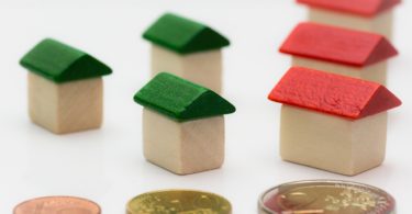 Betriebskosten Nebenkosten als Münzen verteilt vor Miniaturhäusern