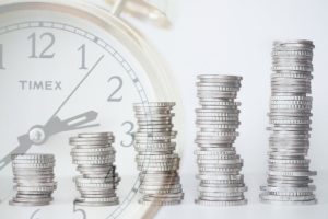 Fünf größer werdende Münzstapel mit Uhr im Hintergrund für steigenden Wert beim Lebensversicherung kündigen