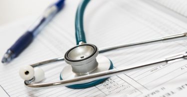 Stethoskop und blauer Kugelschreiber auf Unterlagen zur Krankenzusatzversicherung